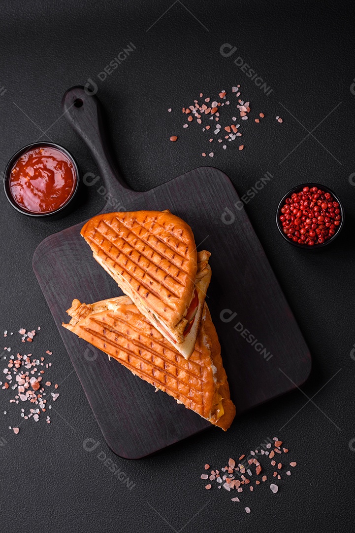 Delicioso sanduíche crocante com peito de frango, tomate, ketchup e especiarias em um fundo escuro de concreto