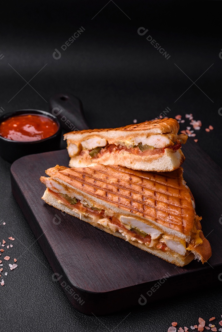 Delicioso sanduíche crocante com peito de frango, tomate, ketchup e especiarias em um fundo escuro de concreto