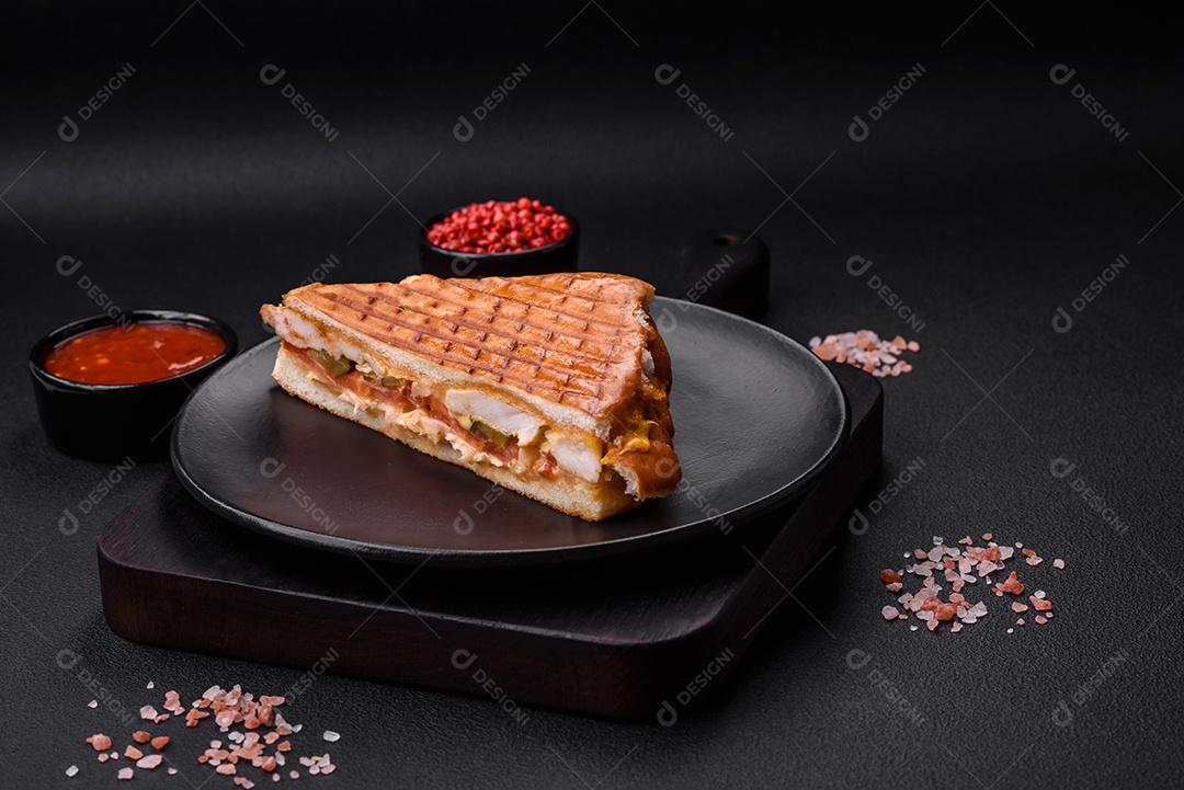 Delicioso sanduíche crocante com peito de frango, tomate, ketchup e especiarias em um fundo escuro de concreto