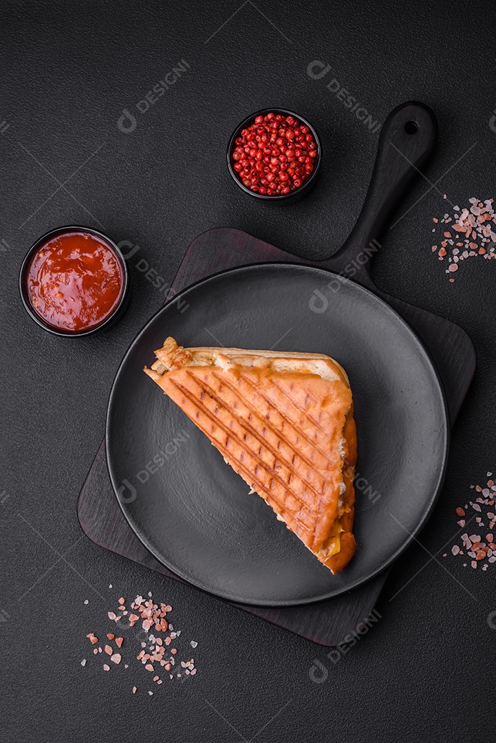 Delicioso sanduíche crocante com peito de frango, tomate, ketchup e especiarias em um fundo escuro de concreto