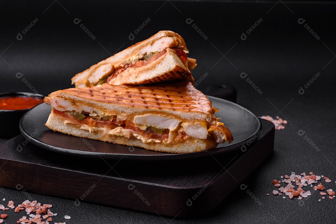 Delicioso sanduíche crocante com peito de frango, tomate, ketchup e especiarias em um fundo escuro de concreto