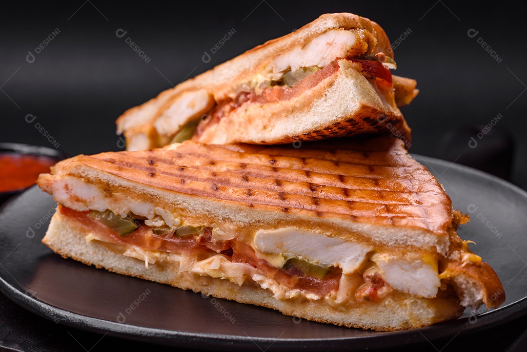 Delicioso sanduíche crocante com peito de frango, tomate, ketchup e especiarias em um fundo escuro de concreto