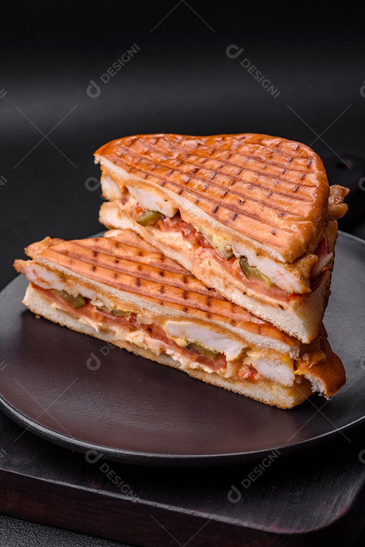 Delicioso sanduíche crocante com peito de frango, tomate, ketchup e especiarias em um fundo escuro de concreto