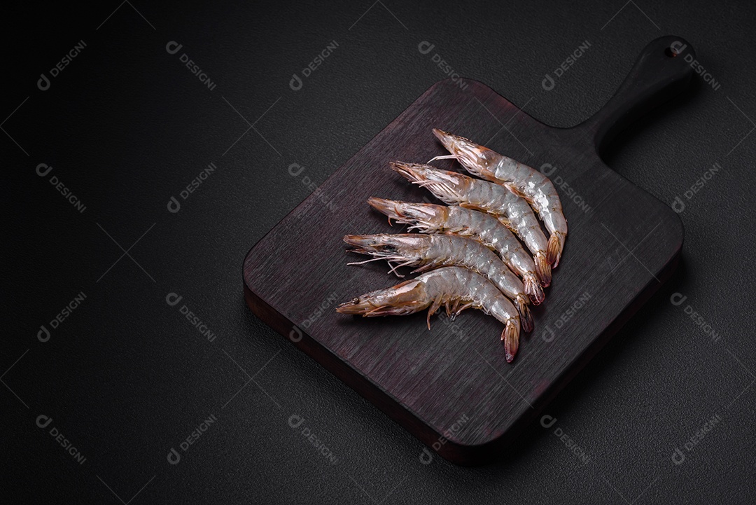 Camarão tigre ou lagostim cru com especiarias e sal em uma tábua de madeira sobre um fundo escuro de concreto