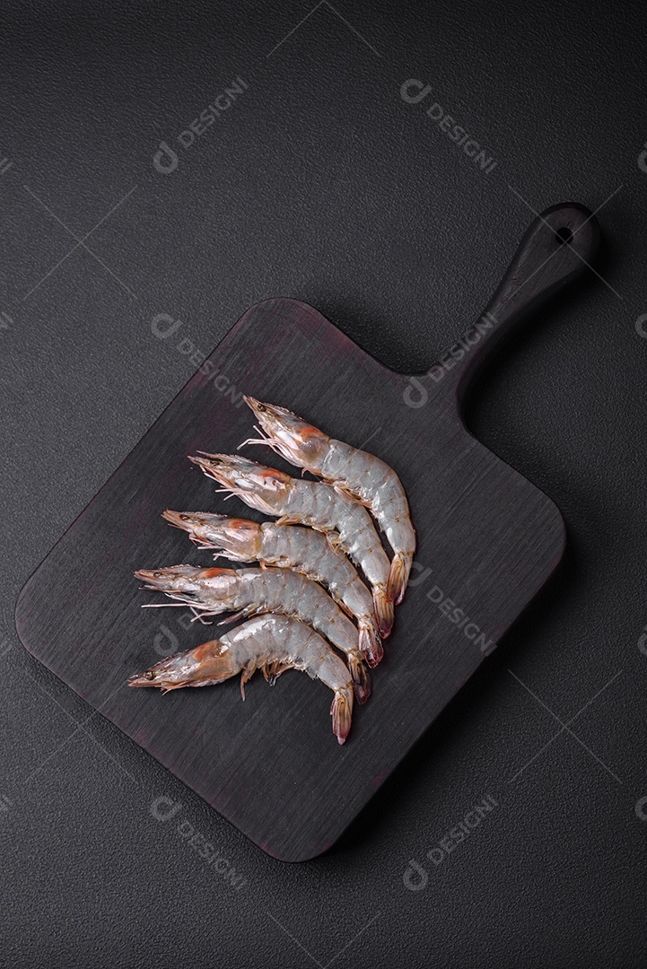 Camarão tigre ou lagostim cru com especiarias e sal em uma tábua de madeira sobre um fundo escuro de concreto