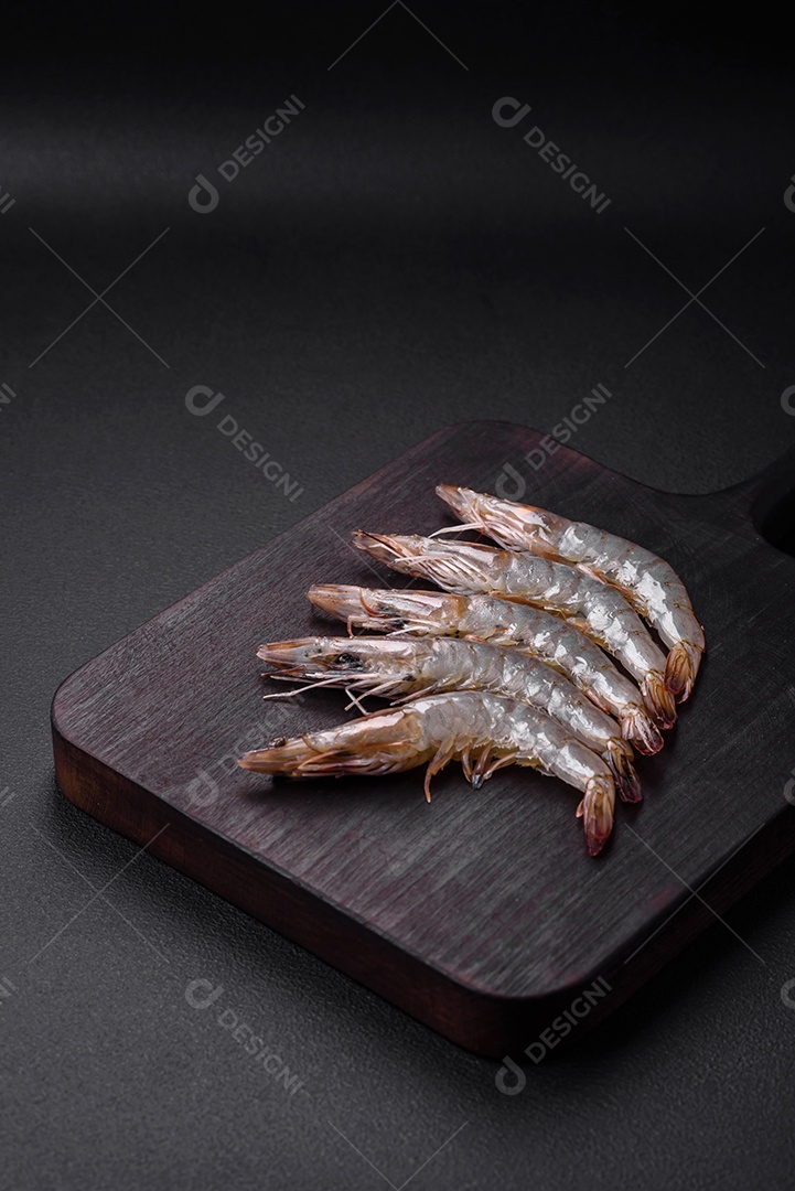 Camarão tigre ou lagostim cru com especiarias e sal em uma tábua de madeira sobre um fundo escuro de concreto