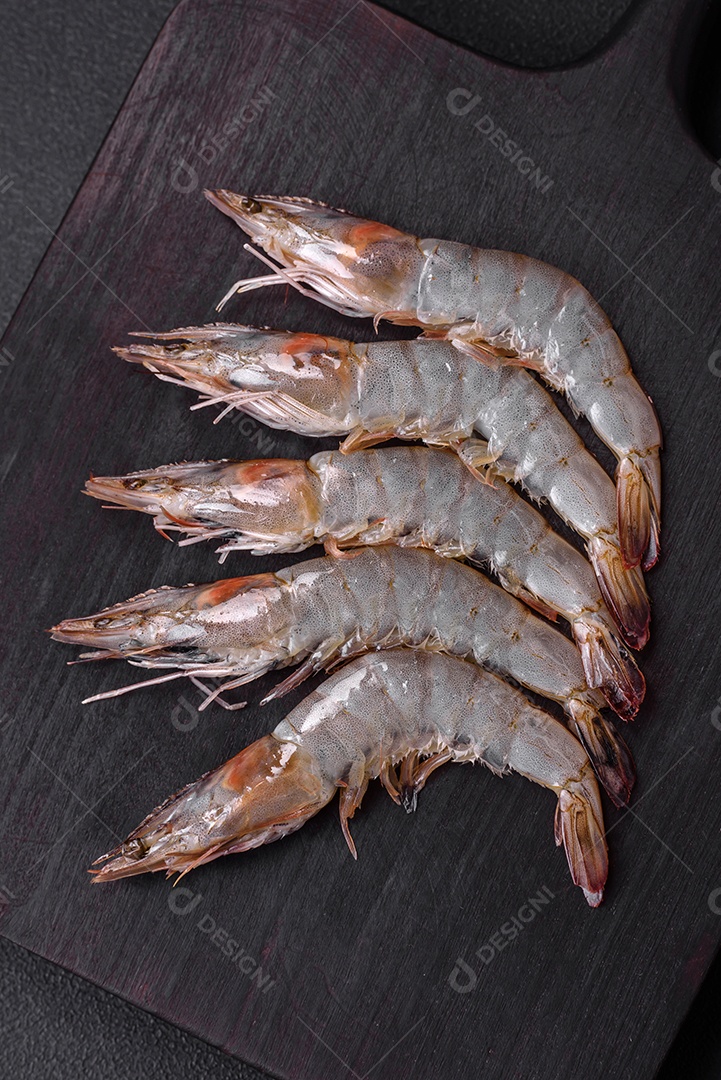 Camarão tigre ou lagostim cru com especiarias e sal em uma tábua de madeira sobre um fundo escuro de concreto