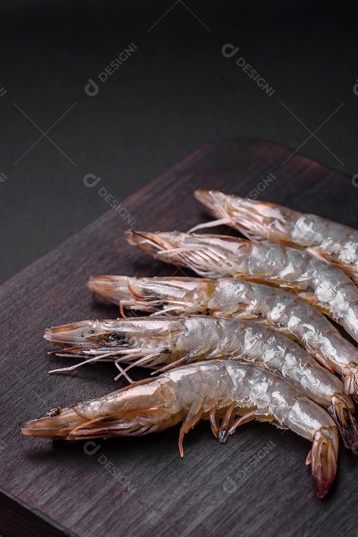 Camarão tigre ou lagostim cru com especiarias e sal em uma tábua de madeira sobre um fundo escuro de concreto