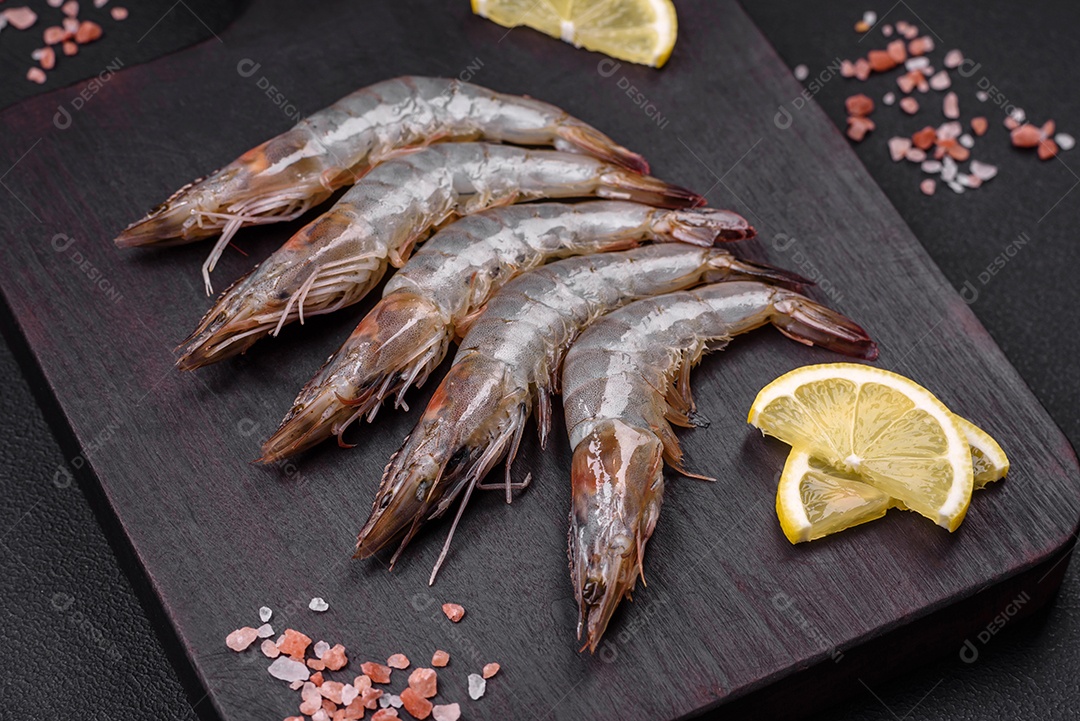 Camarão tigre ou lagostim cru com especiarias e sal em uma tábua de madeira sobre um fundo escuro de concreto