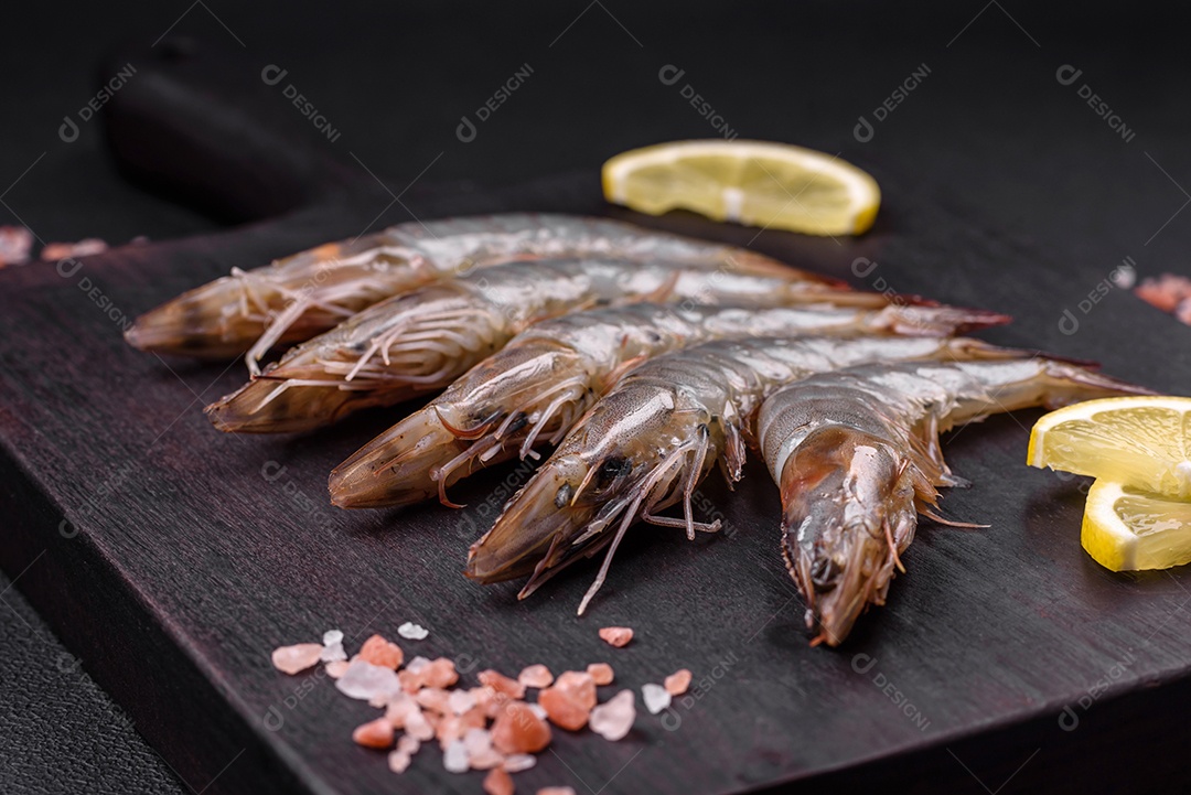 Camarão tigre ou lagostim cru com especiarias e sal em uma tábua de madeira sobre um fundo escuro de concreto