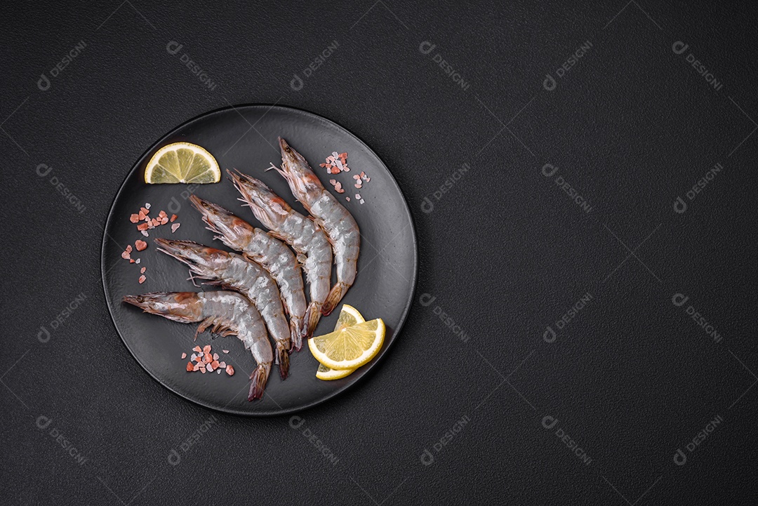 Camarão tigre ou lagostim cru com especiarias e sal em uma tábua de madeira sobre um fundo escuro de concreto