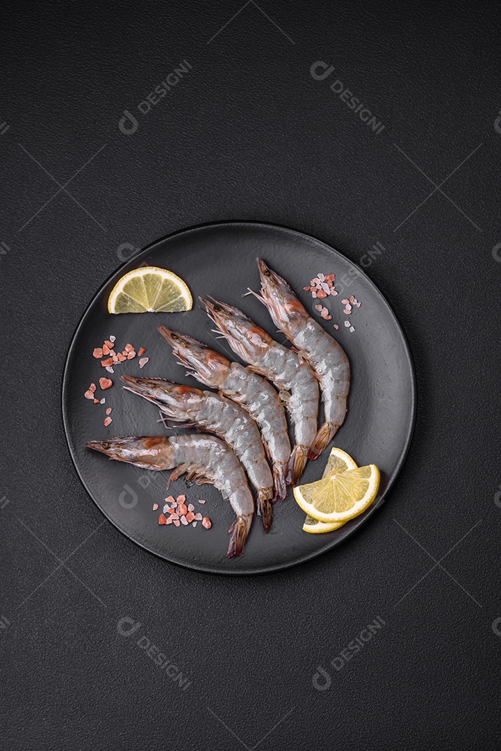 Camarão tigre ou lagostim cru com especiarias e sal em uma tábua de madeira sobre um fundo escuro de concreto