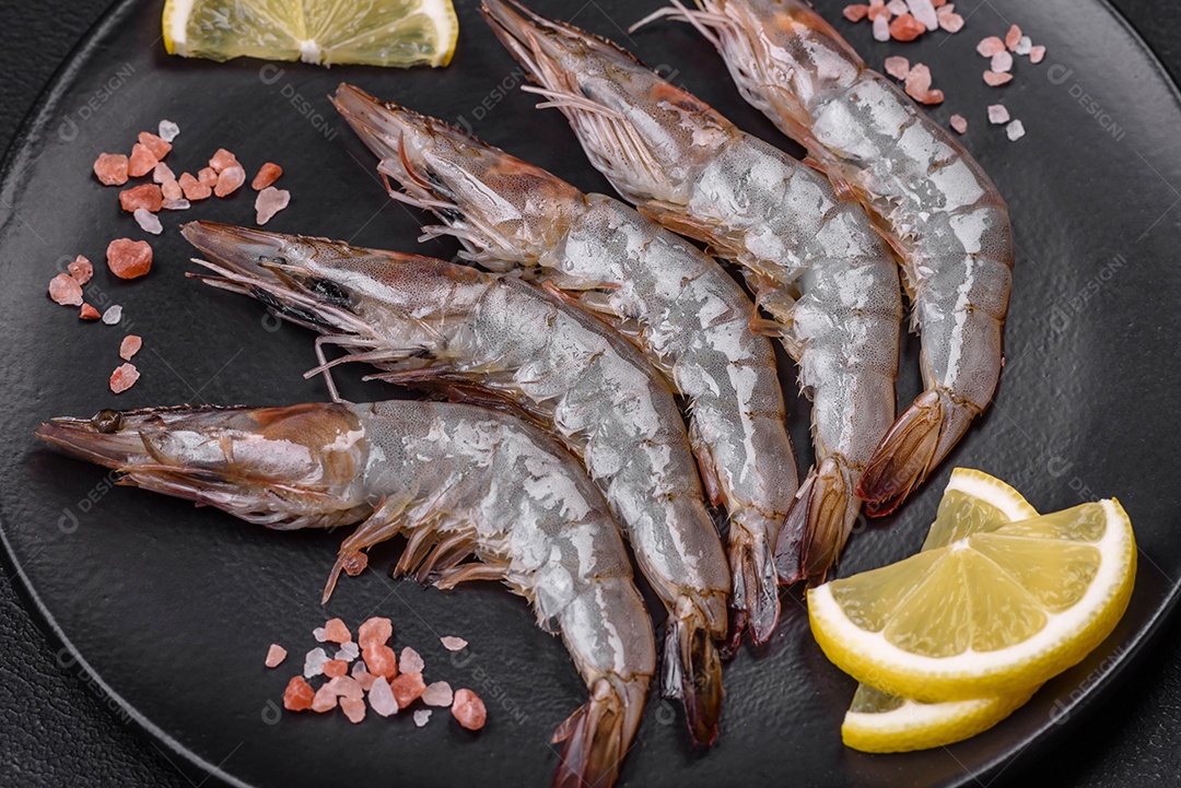 Camarão tigre ou lagostim cru com especiarias e sal em uma tábua de madeira sobre um fundo escuro de concreto