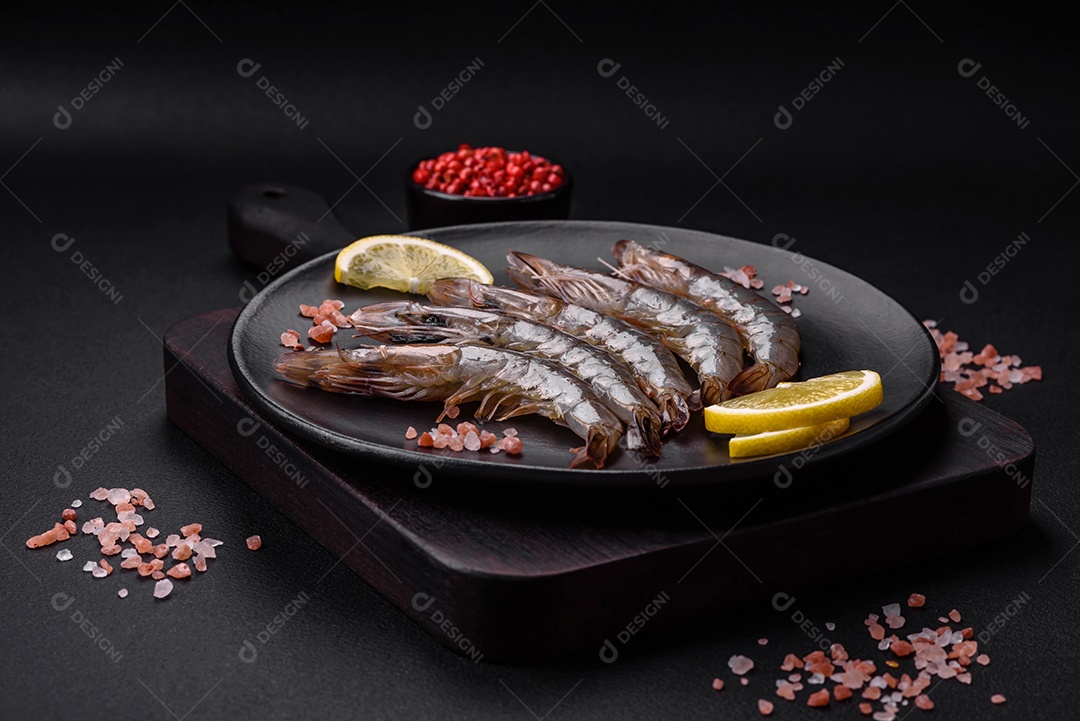 Camarão tigre ou lagostim cru com especiarias e sal em uma tábua de madeira sobre um fundo escuro de concreto