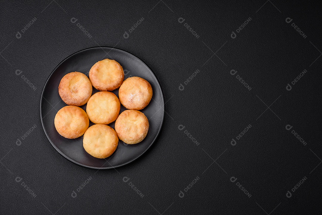 Deliciosos cheesecakes frescos com passas e baunilha em uma placa de cerâmica preta sobre um fundo escuro de concreto