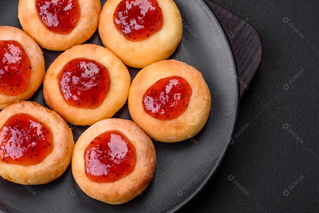 Deliciosos biscoitos frescos com geleia de goiaba em uma placa de cerâmica preta sobre um fundo escuro de concreto