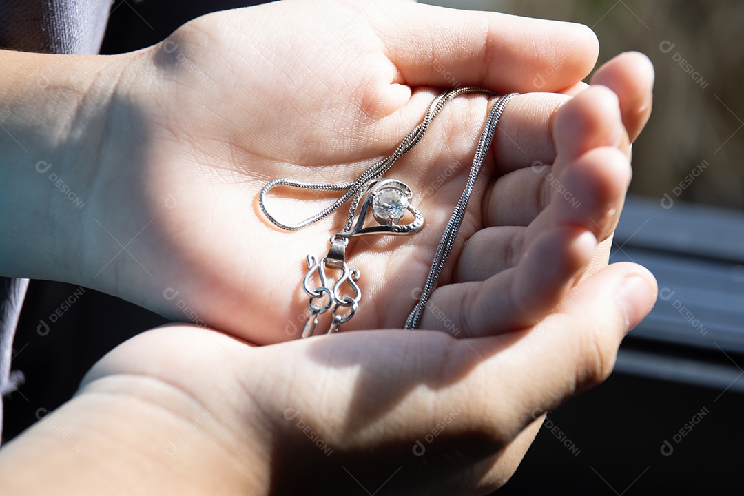 Mão de mulher gentil segurando um colar de diamantes prateados