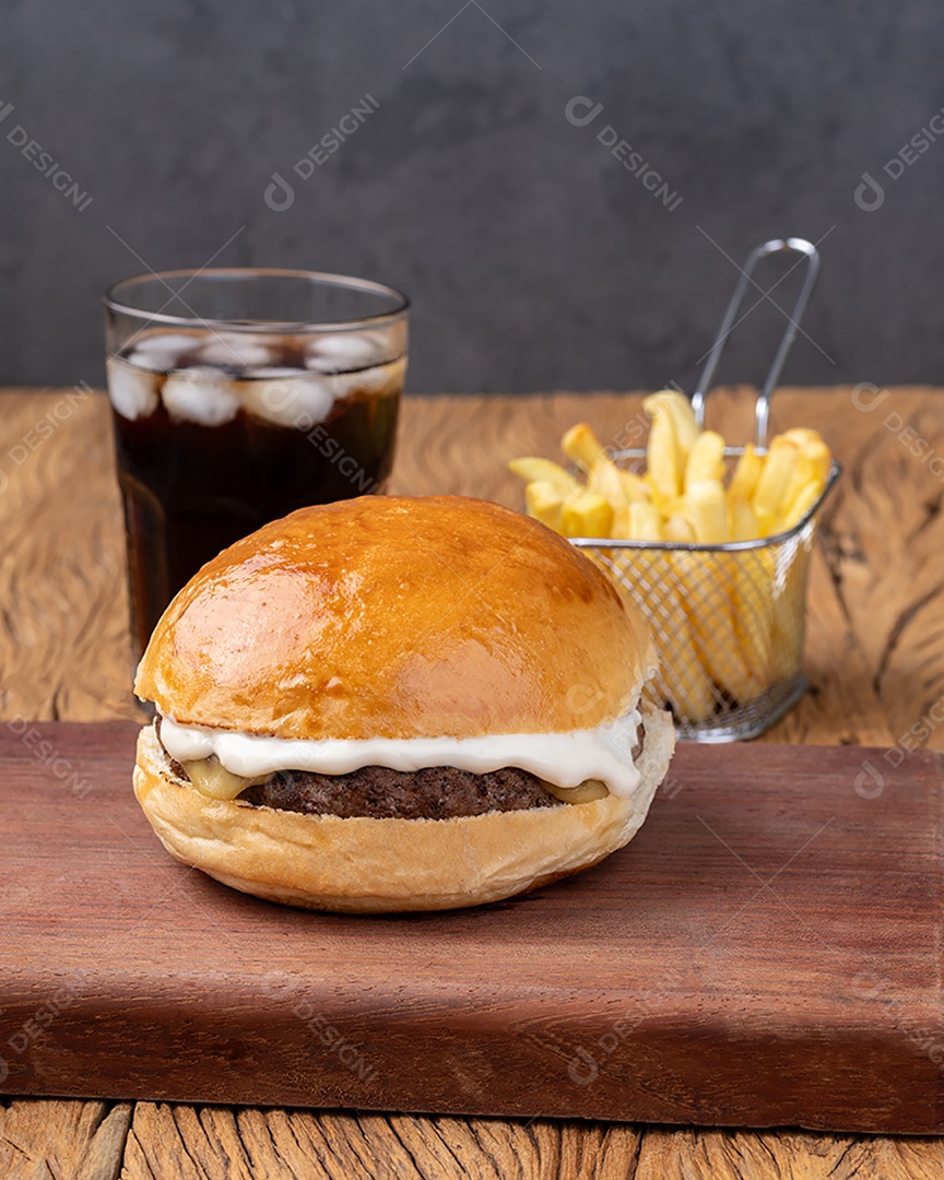 Cheeseburger com maionese sobre tábua de madeira com batata frita e refrigerante.