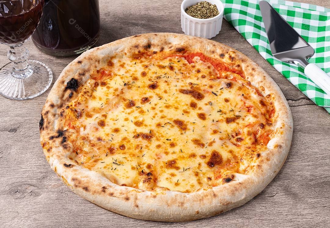 Pizza estilo queijo mussarela sobre mesa de madeira com vinho, orégano e espátula.