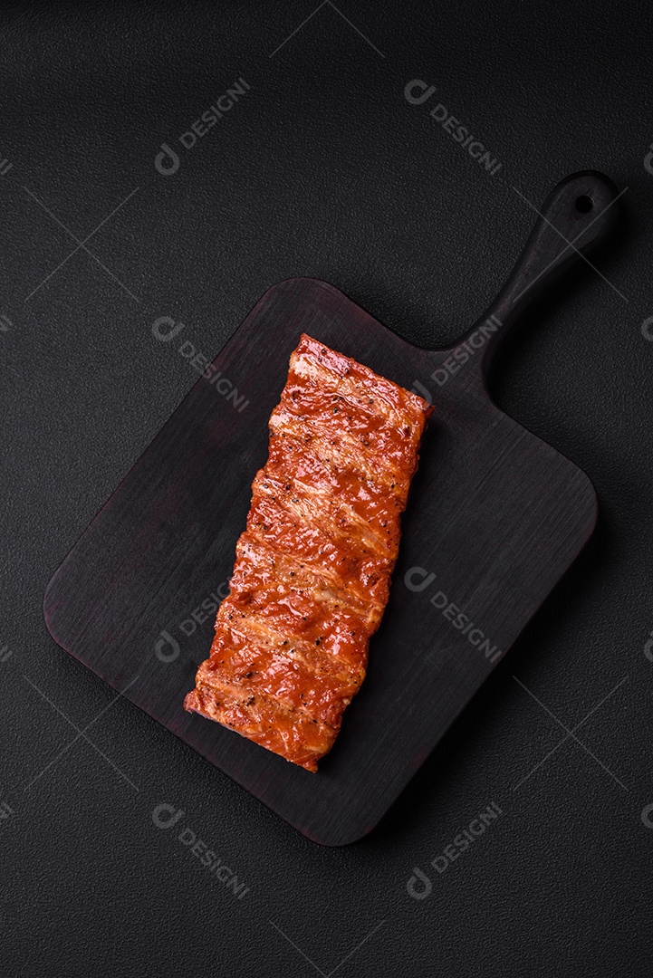 Deliciosas costelas frescas grelhadas ou defumadas com sal, especiarias e ervas em fundo escuro de concretoDeliciosas costelas frescas grelhadas ou defumadas com sal, especiarias e ervas em fundo escuro de concreto
