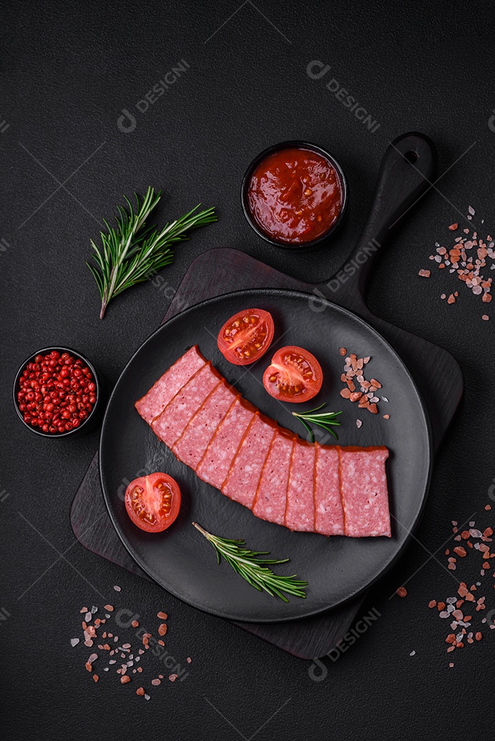 Delicioso salame de salsicha fresca com sal, tomate e especiarias sobre um fundo escuro de concreto