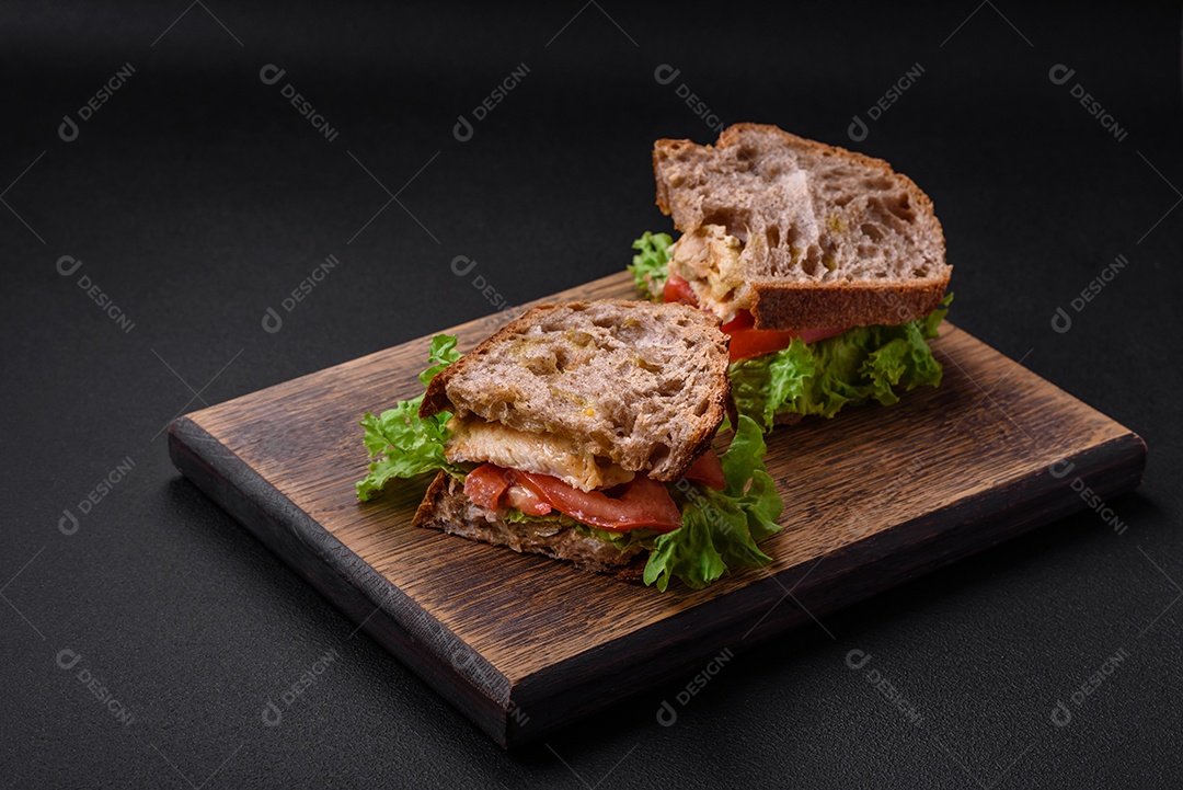 Delicioso sanduíche com torradas crocantes, frango, tomate e alface sobre fundo escuro de concreto