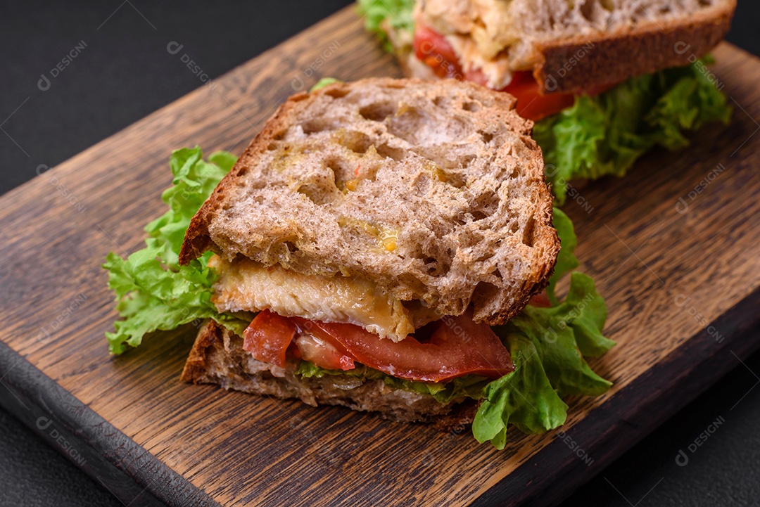 Delicioso sanduíche com torradas crocantes, frango, tomate e alface sobre fundo escuro de concreto