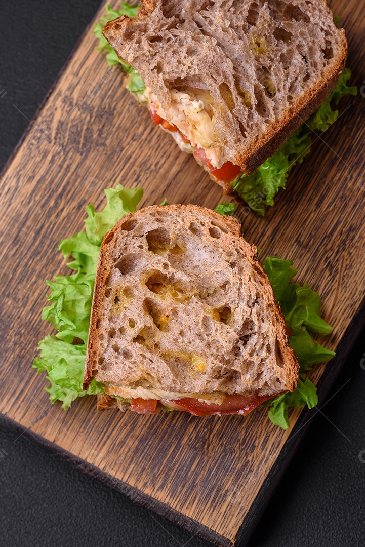 Delicioso sanduíche com torradas crocantes, frango, tomate e alface sobre fundo escuro de concreto