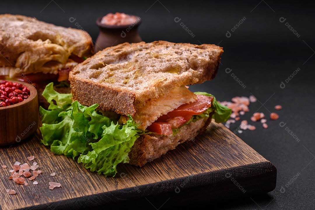 Delicioso sanduíche com torradas crocantes, frango, tomate e alface sobre fundo escuro de concreto