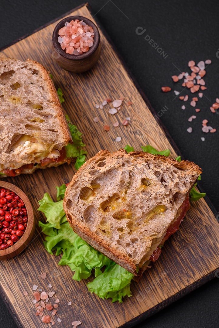 Delicioso sanduíche com torradas crocantes, frango, tomate e alface sobre fundo escuro de concreto