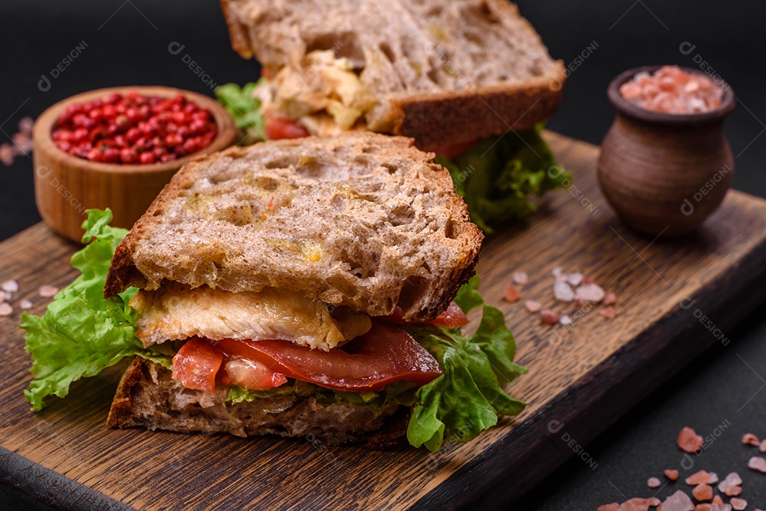 Delicioso sanduíche com torradas crocantes, frango, tomate e alface sobre fundo escuro de concreto