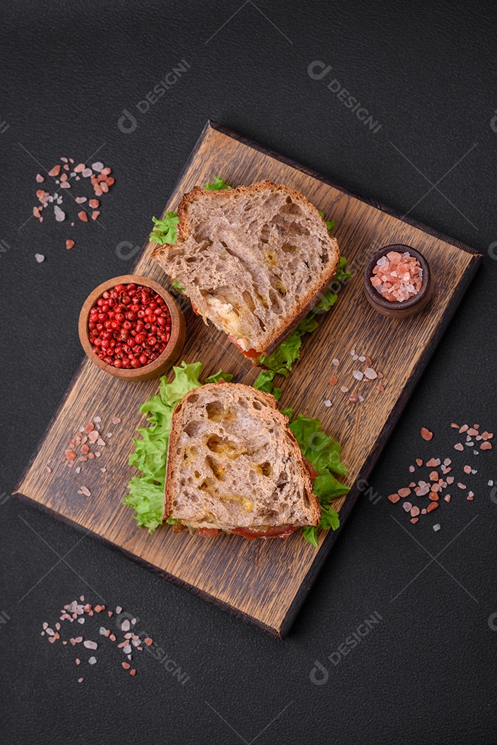 Delicioso sanduíche com torradas crocantes, frango, tomate e alface sobre fundo escuro de concreto