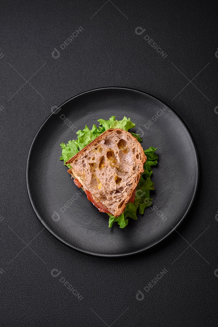 Delicioso sanduíche com torradas crocantes, frango, tomate e alface sobre fundo escuro de concreto