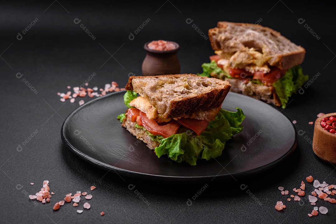 Delicioso sanduíche com torradas crocantes, frango, tomate e alface sobre fundo escuro de concreto