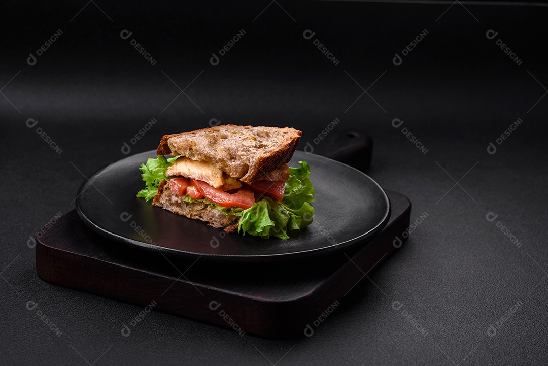 Delicioso sanduíche com torradas crocantes, frango, tomate e alface sobre fundo escuro de concreto