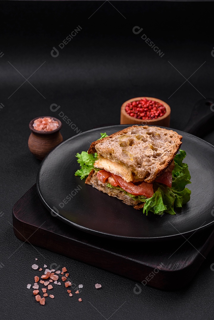 Delicioso sanduíche com torradas crocantes, frango, tomate e alface sobre fundo escuro de concreto