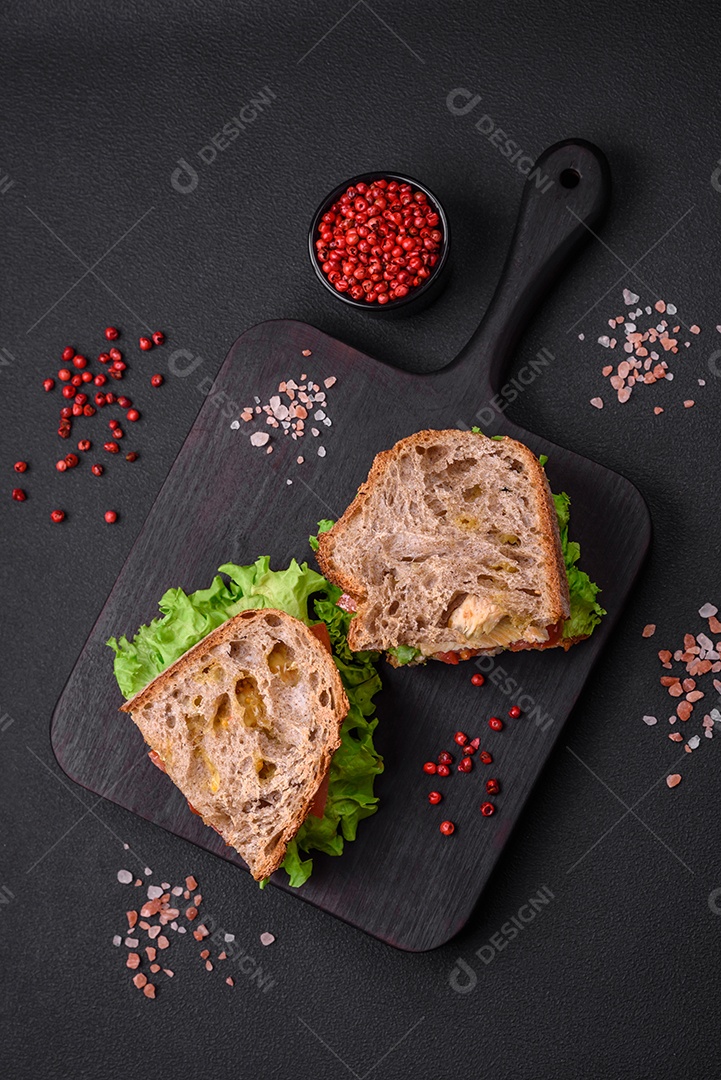 Delicioso sanduíche com torradas crocantes, frango, tomate e alface sobre fundo escuro de concreto