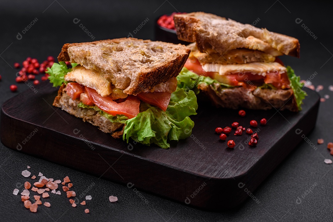 Delicioso sanduíche com torradas crocantes, frango, tomate e alface sobre fundo escuro de concreto