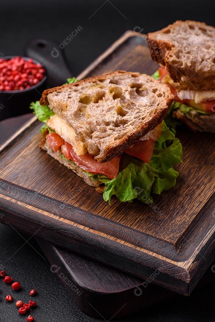 Delicioso sanduíche com torradas crocantes, frango, tomate e alface sobre fundo escuro de concreto