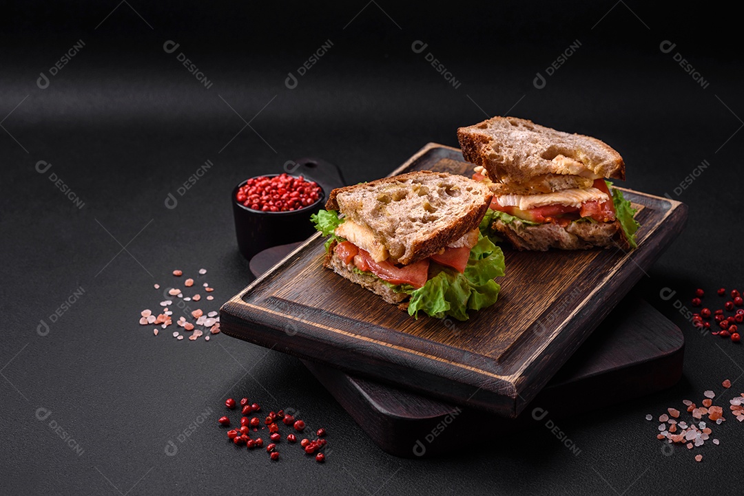 Delicioso sanduíche com torradas crocantes, frango, tomate e alface sobre fundo escuro de concreto
