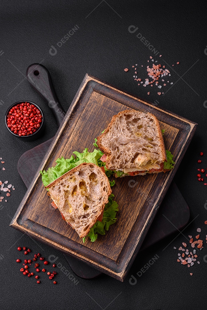 Delicioso sanduíche com torradas crocantes, frango, tomate e alface sobre fundo escuro de concreto