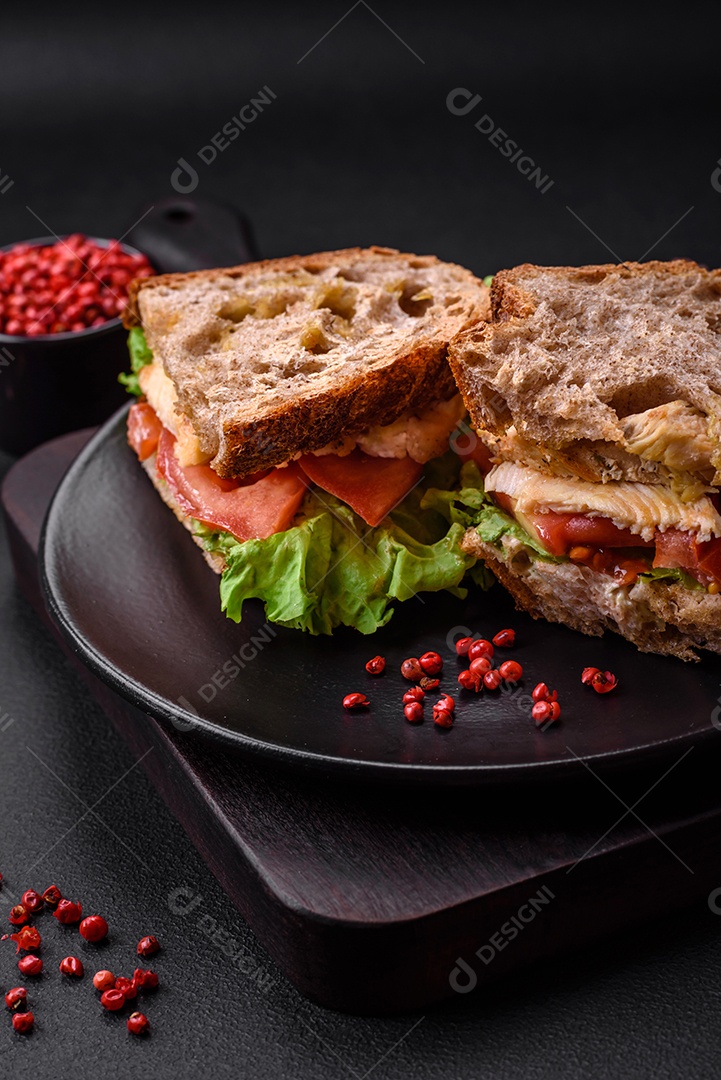 Delicioso sanduíche com torradas crocantes, frango, tomate e alface sobre fundo escuro de concreto