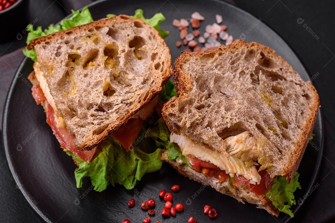 Delicioso sanduíche com torradas crocantes, frango, tomate e alface sobre fundo escuro de concreto