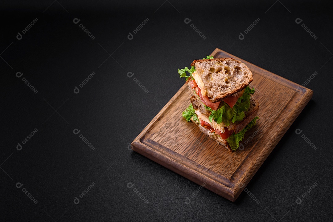 Delicioso sanduíche com torradas crocantes, frango, tomate e alface sobre fundo escuro de concreto