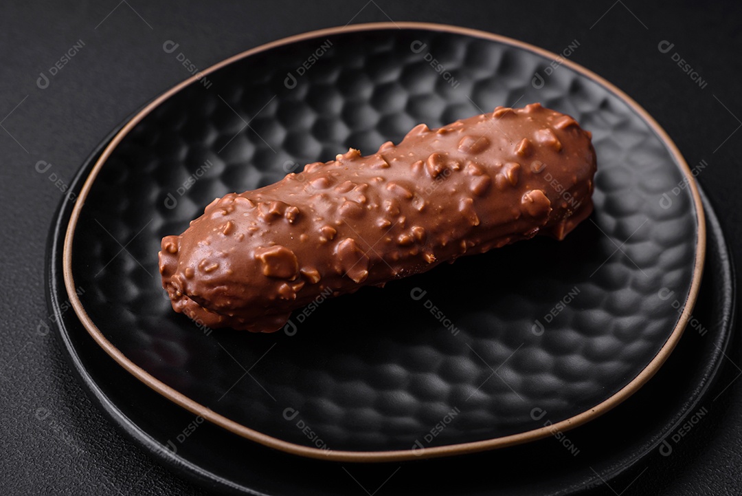 Delicioso bolo éclair fresco ou profiterole com chocolate e nozes sobre um fundo escuro de concreto
