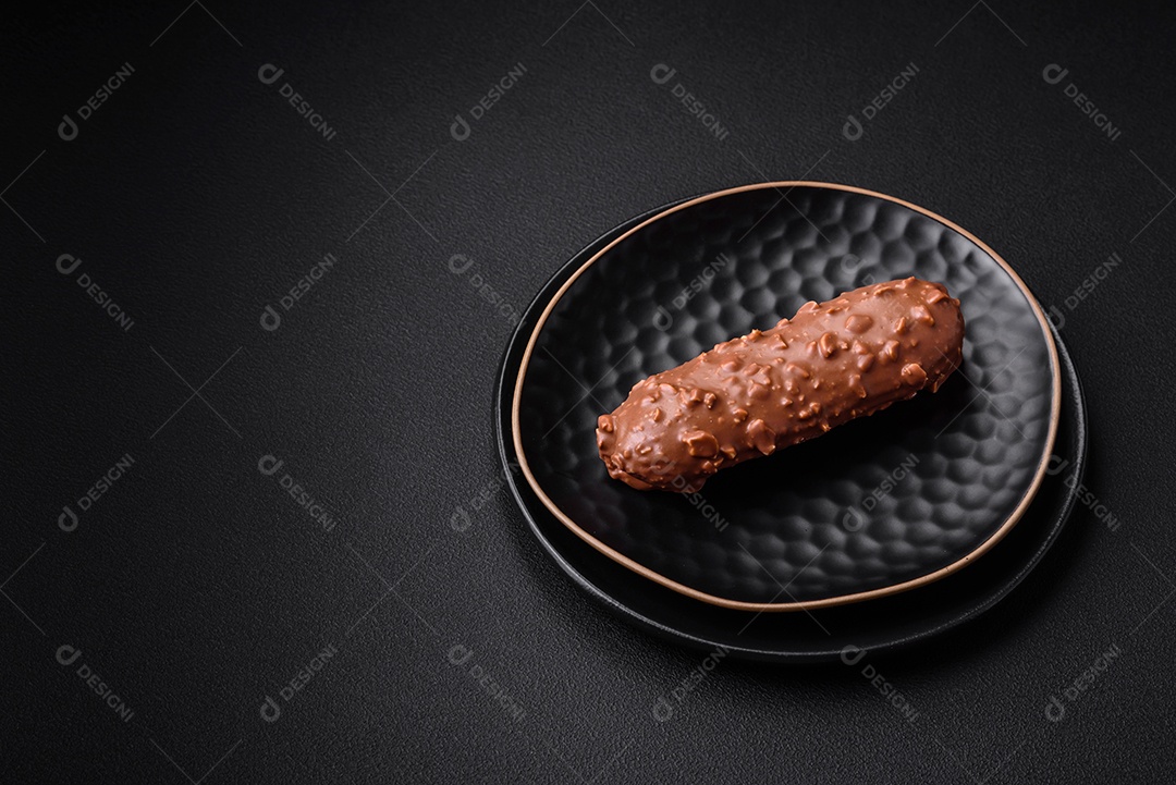 Delicioso bolo éclair fresco ou profiterole com chocolate e nozes sobre um fundo escuro de concreto