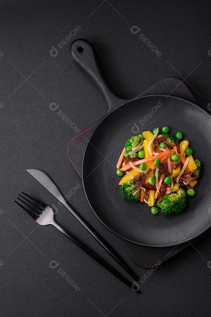 Deliciosos legumes cozidos no vapor, brócolis, cogumelos, ervilhas, cenouras e cebolas sobre um fundo escuro de concreto