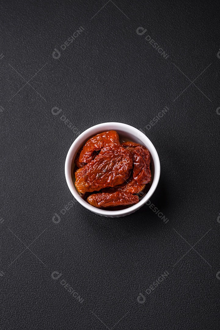 Deliciosos tomates secos ao sol em óleo numa tigela de cerâmica branca sobre um fundo escuro de concreto