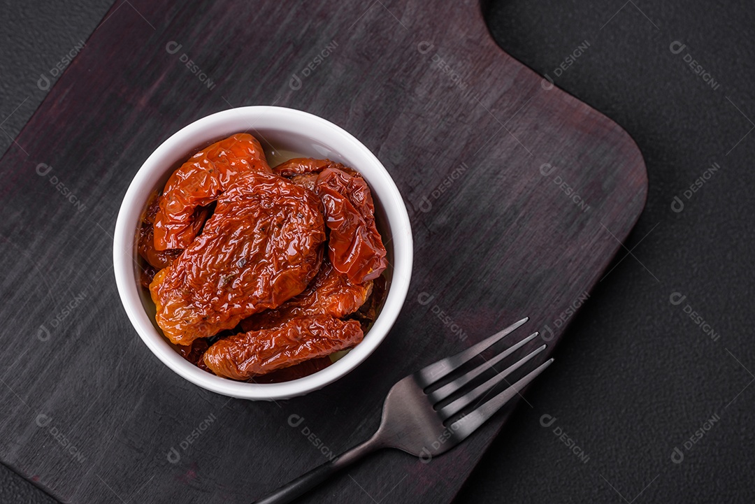 Deliciosos tomates secos ao sol em óleo numa tigela de cerâmica branca sobre um fundo escuro de concreto