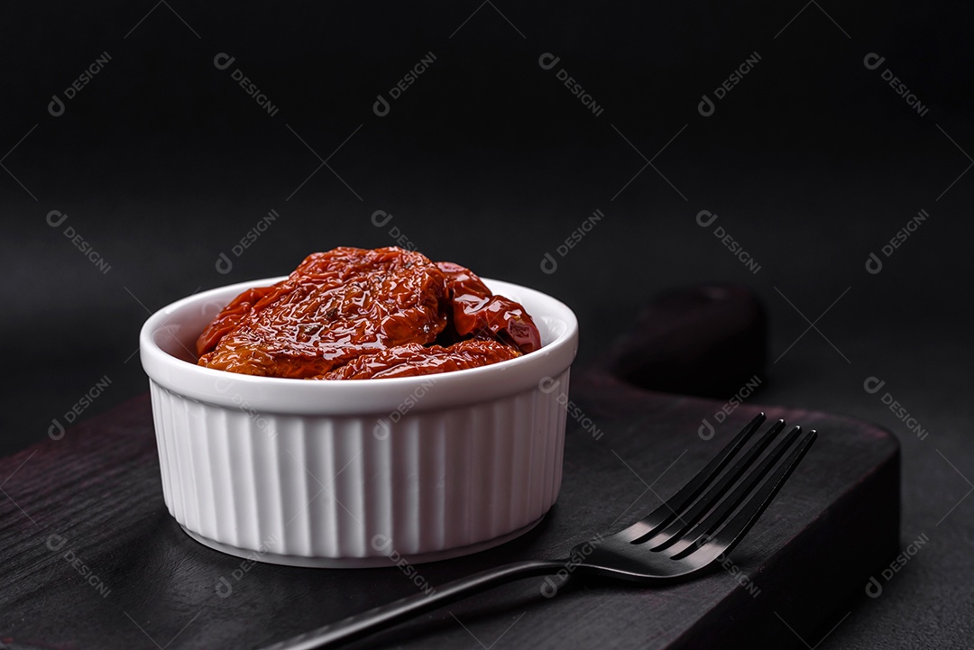 Deliciosos tomates secos ao sol em óleo numa tigela de cerâmica branca sobre um fundo escuro de concreto